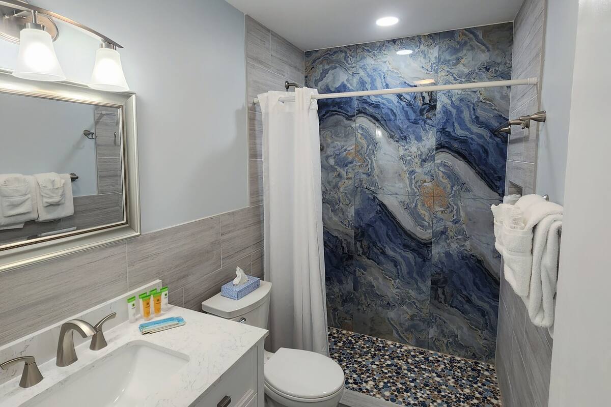 A modern bathroom with a marble shower wall, a white sink with a marble countertop, and a toilet with a marble-patterned floor.