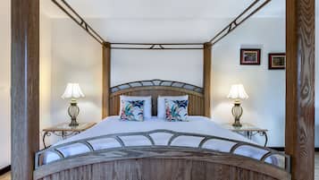 A four-poster bed with a wooden frame and a canopy, two bedside lamps, and two pillows with tropical prints.