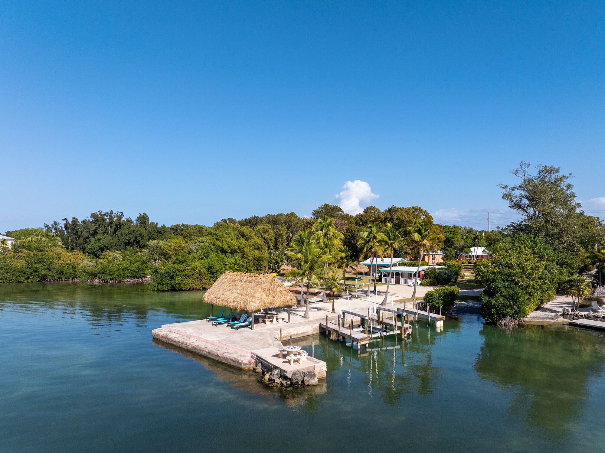 A dock with lounge chairs and a thatched-roof structure, surrounded by lush greenery and a clear blue sky.