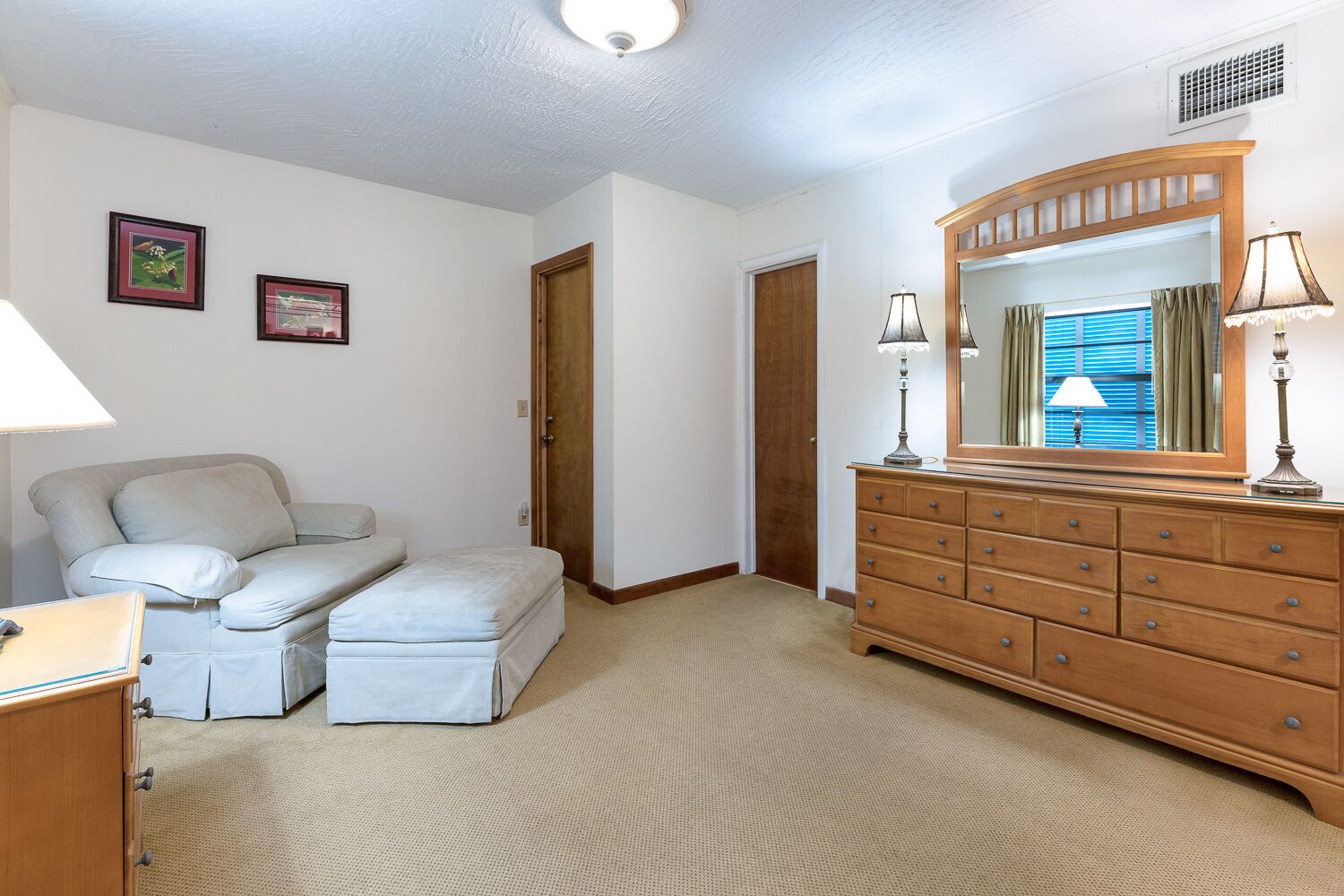 A bedroom with a bed, a dresser, a mirror, and two framed pictures on the wall.