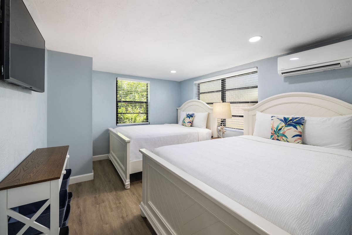 A bedroom with two beds, a desk, and a window with blinds.