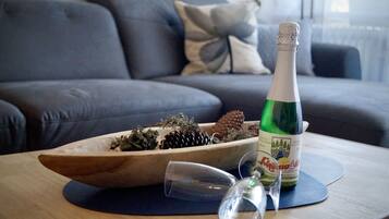 Une bouteille de vin posée sur un dessous de verre, à côté d’un verre et d’un bol en bois contenant des pommes de pin et des éléments de verdure, le tout sur une table.