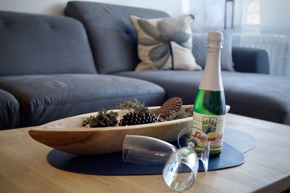 A bottle of wine on a coaster with a glass and a wooden bowl containing pinecones and greenery on a table.