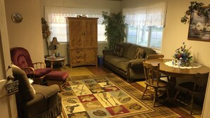 Un salon chaleureux avec un meuble en bois, un canapé, une causeuse, une table à manger avec des chaises et un tapis à motifs.