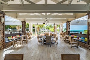A spacious outdoor dining area with wooden tables and chairs, a central round table, and a view of the ocean. - 4BR Key Largo Villa w/ Beach & Marriott Perks (Key Largo)