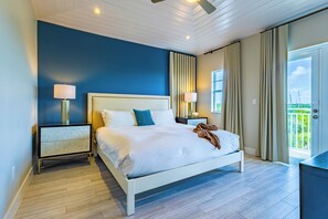 A modern bedroom with a large bed, two bedside tables with lamps, a ceiling fan, and a balcony view. - 4BR Key Largo Villa w/ Beach & Marriott Perks (Key Largo)