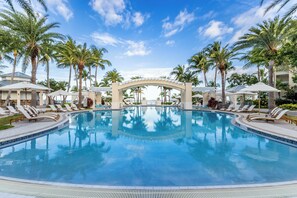 Een groot zwembad met ligbedden en parasols, omringd door palmbomen en een heldere lucht.