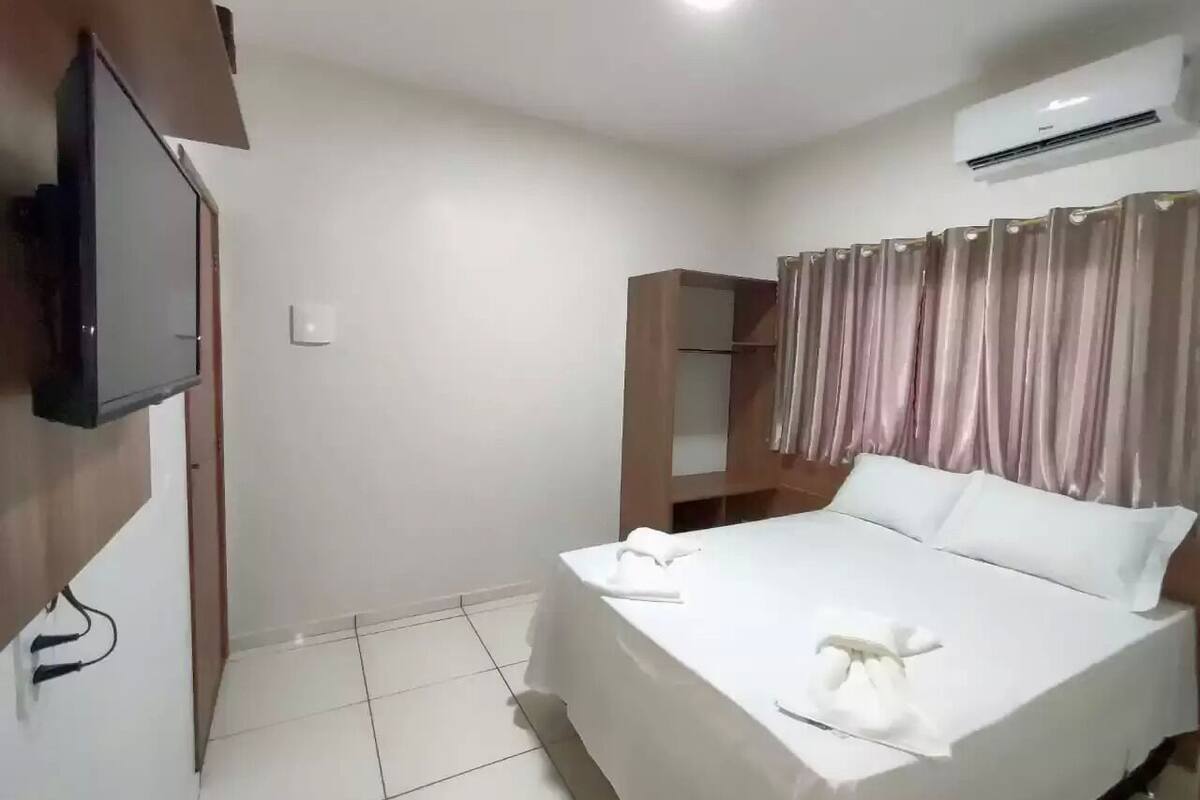 A hotel room with a bed, a television mounted on the wall, a wardrobe, and an air conditioning unit.