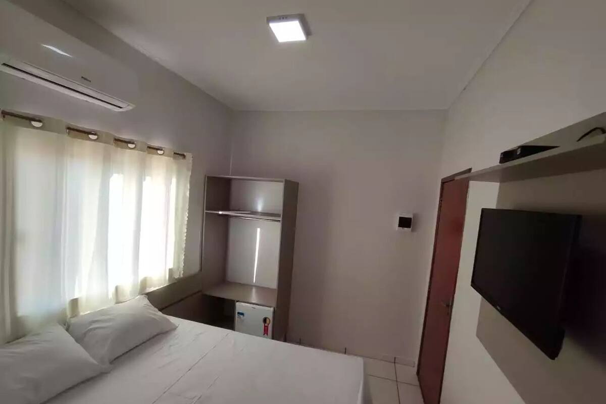A hotel room with a bed, a TV mounted on the wall, a wardrobe, and a small kitchenette area.