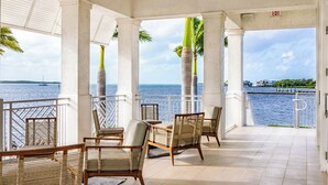 A covered outdoor seating area with wicker chairs and a view of the sea.