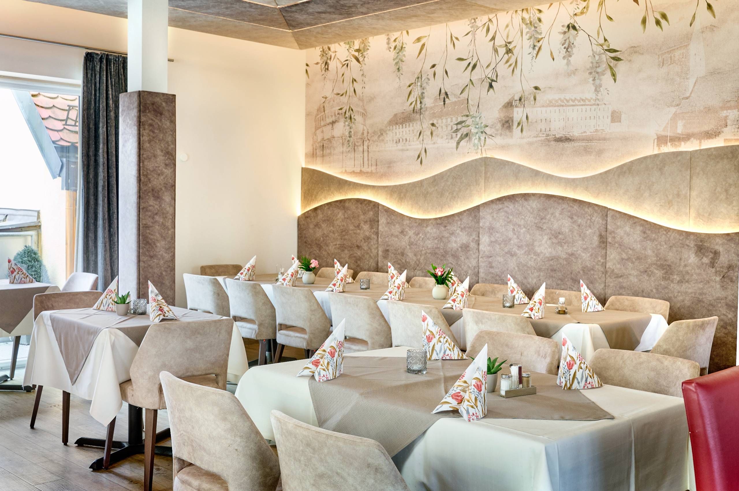 A restaurant with multiple tables, each set with a tablecloth, chairs, and decorative pillows.