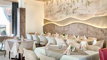 A restaurant with multiple tables, each set with a tablecloth, chairs, and decorative pillows.