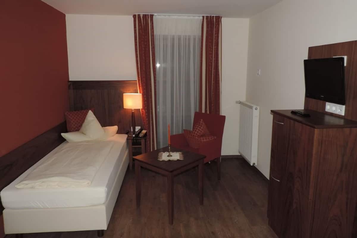 Ein Hotelzimmer mit Bett, Schreibtisch, Stuhl, Fernseher und einem Fenster mit Vorhängen.