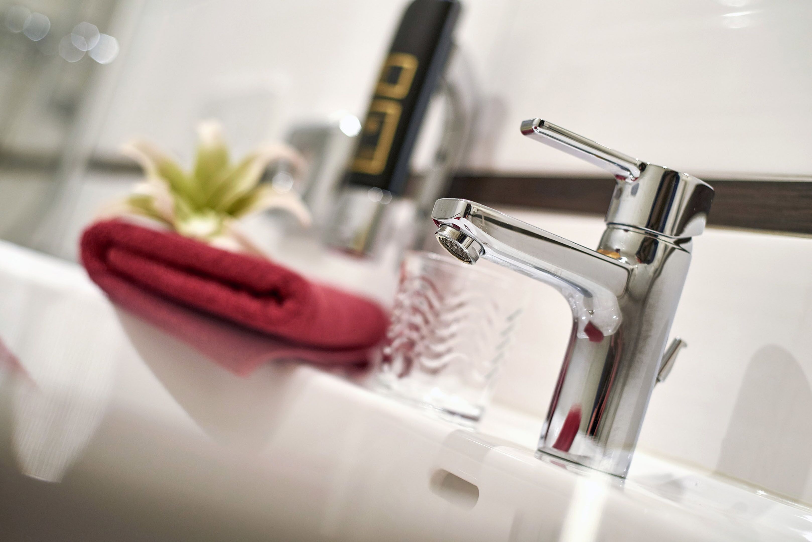 A modern bathroom with a chrome faucet, a glass container, and a red towel.
