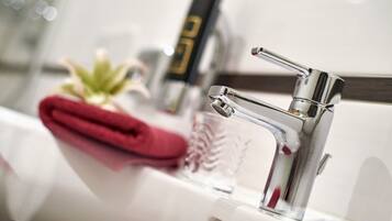 A modern bathroom with a chrome faucet, a glass container, and a red towel.