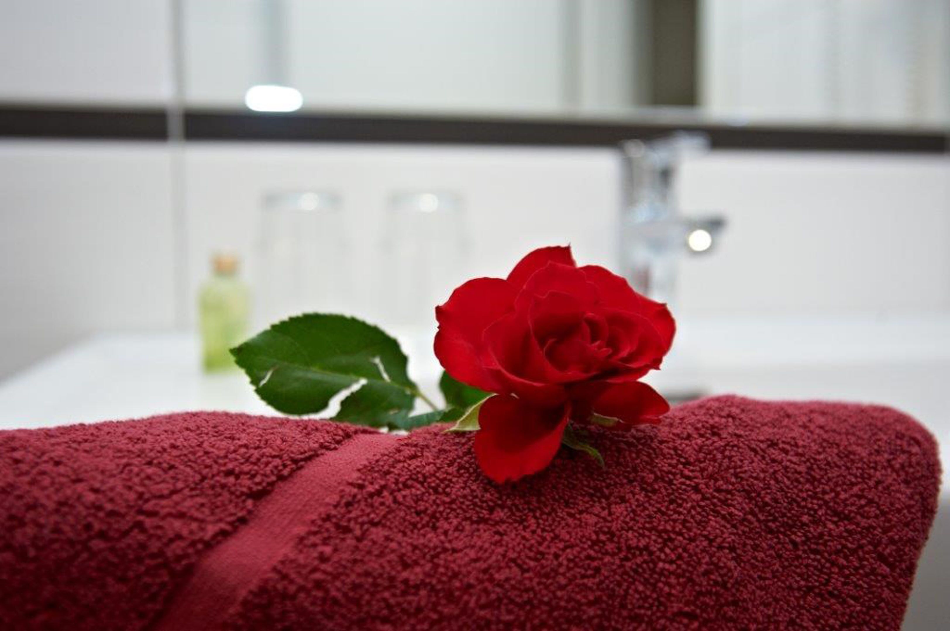 Una toalla roja con una rosa, una botella de loción y un espejo en un baño.