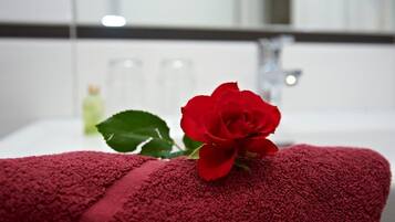 Una toalla roja con una rosa, una botella de loción y un espejo en un baño.
