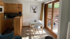 A compact kitchen with wooden cabinets, a dining table with chairs, and a large window with a view of the outdoors.