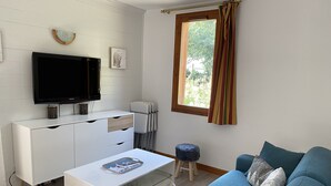 A modern living room with a flat-screen TV, white furniture, a blue sofa, and a window with curtains.