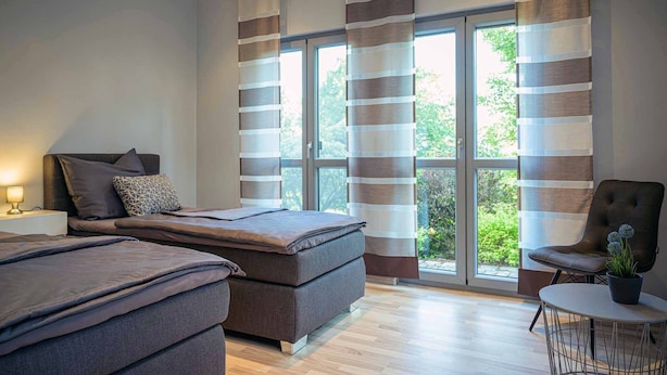 Un dormitorio moderno con dos camas, una zona de estar y ventanas grandes con cortinas a rayas.