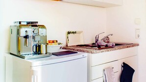 Una kitchenette compacta equipada con cafetera, tostadora, refrigerador pequeño y lavamanos con grifo.