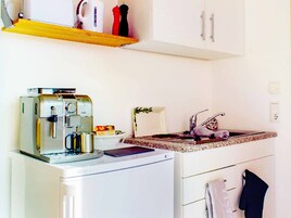 A compact kitchenette with a coffee maker, a toaster, a small refrigerator, and a sink with a faucet.