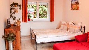 Un dormitorio con cama, sofá rojo, cómoda de madera, ventana con cortinas y un cuadro en la pared.