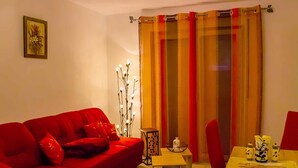 Una sala de estar con un sofá rojo, una mesita con objetos decorativos y una cortina con rayas verticales.