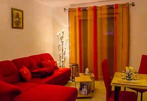 A living room with a red sofa, a small table with decorative items, and a curtain with vertical stripes.