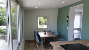 A dining area with a wooden table and chairs, a window with a view of greenery, and a built-in induction cooktop. - The Provençal villa. (Sarrians)