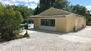 A small, single-story building with a tiled roof, a large window, and a gravel driveway. - The Provençal villa. (Sarrians)