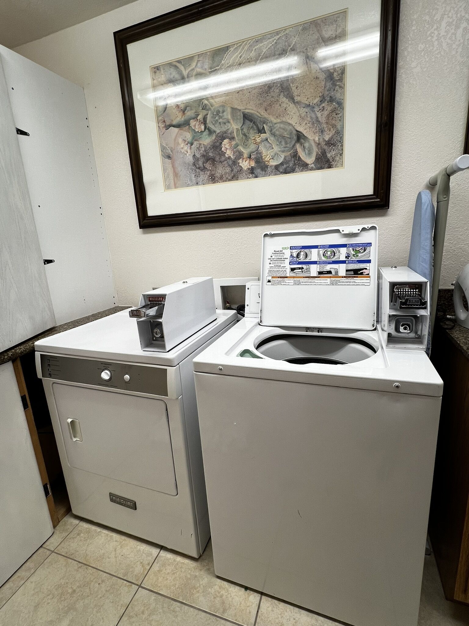 Une buanderie équipée d’un lave-linge et d’un sèche-linge à chargement frontal, d’une œuvre d’art encadrée au mur et d’un petit panneau de commande.