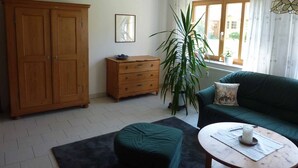 A room with a wooden wardrobe, a green sofa, a round table, and a large potted plant. - Ferienwohnung Fantaisie (Eckersdorf)