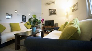 Uma sala de estar com sofá, mesa de centro, televisão e planta.