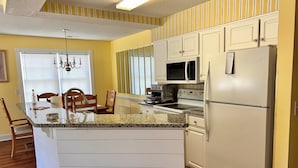 A kitchen with white cabinets, a granite countertop, a refrigerator, a microwave, a toaster, and a chandelier. - Nice apartment with golf course view in prestigious Brunswick Golf. Fits 4.  (Calabash)