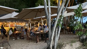 Un restaurant situé en bord de mer, avec une terrasse, des tables en bois et des parasols.