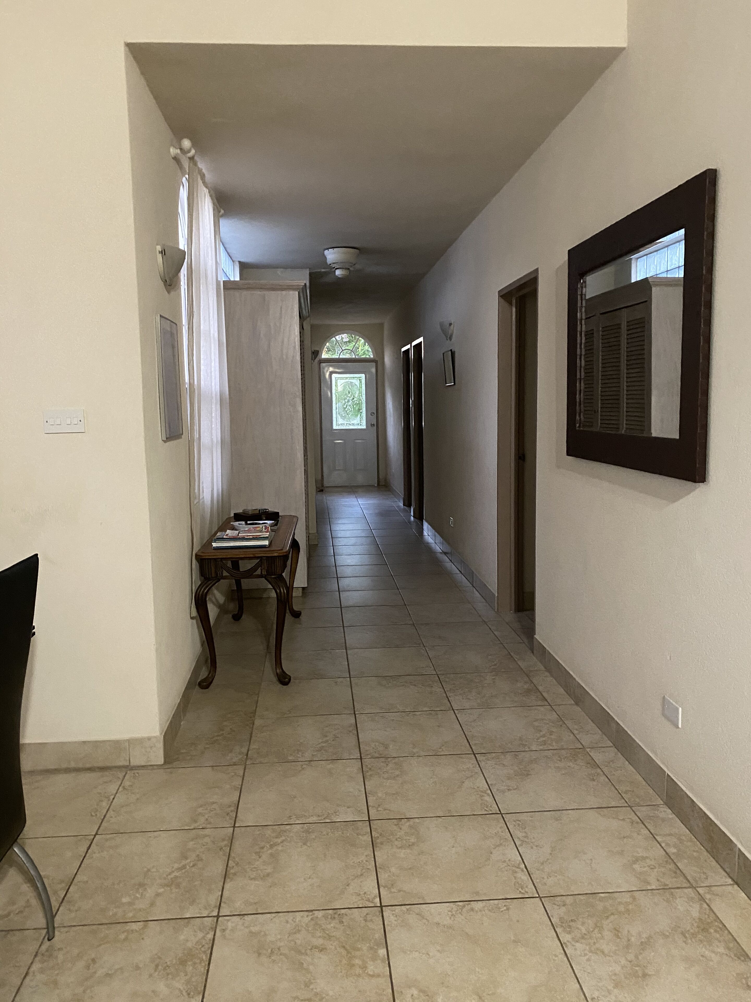 A hallway with a tiled floor, a table with books, and a door at the end.