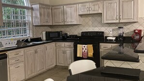 Une cuisine avec des meubles de couleur bois clair, un plan de travail noir, un ventilateur de plafond et une fenêtre donnant sur des arbres.