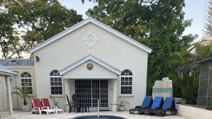 Une piscine dotée de deux échelles en métal, entourée de chaises longues et bordée d’un bâtiment aux fenêtres en arc et orné d’un motif solaire.
