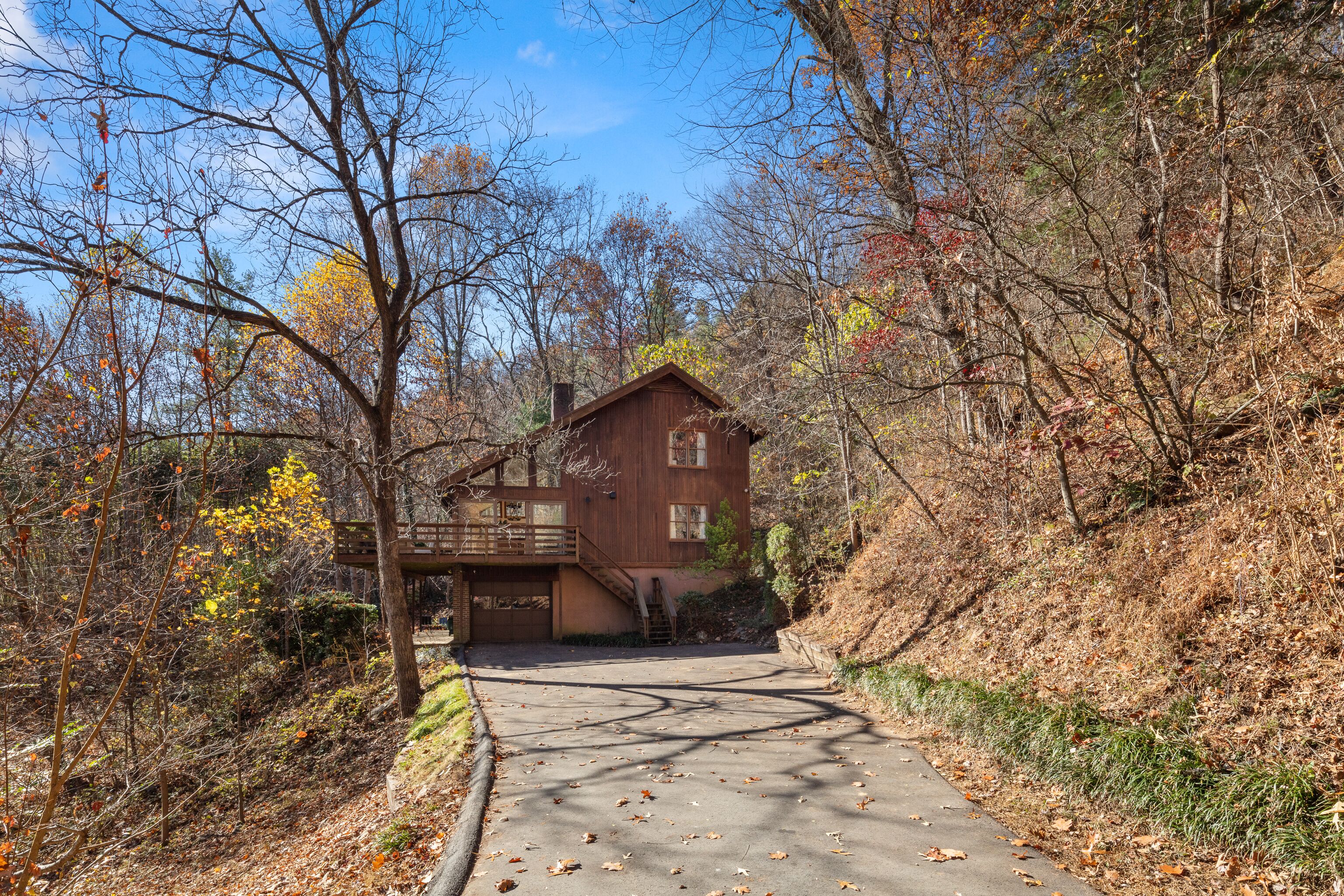 A rustic cabin with a wooden exterior, a covered porch, and a paved driveway leading to the entrance.