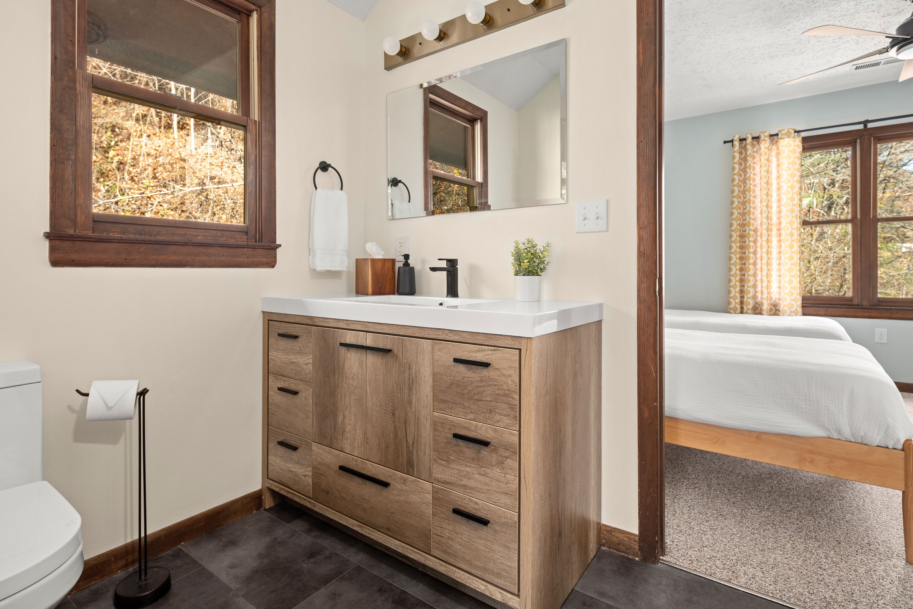 Un baño con tocador de madera, espejo y ventana.