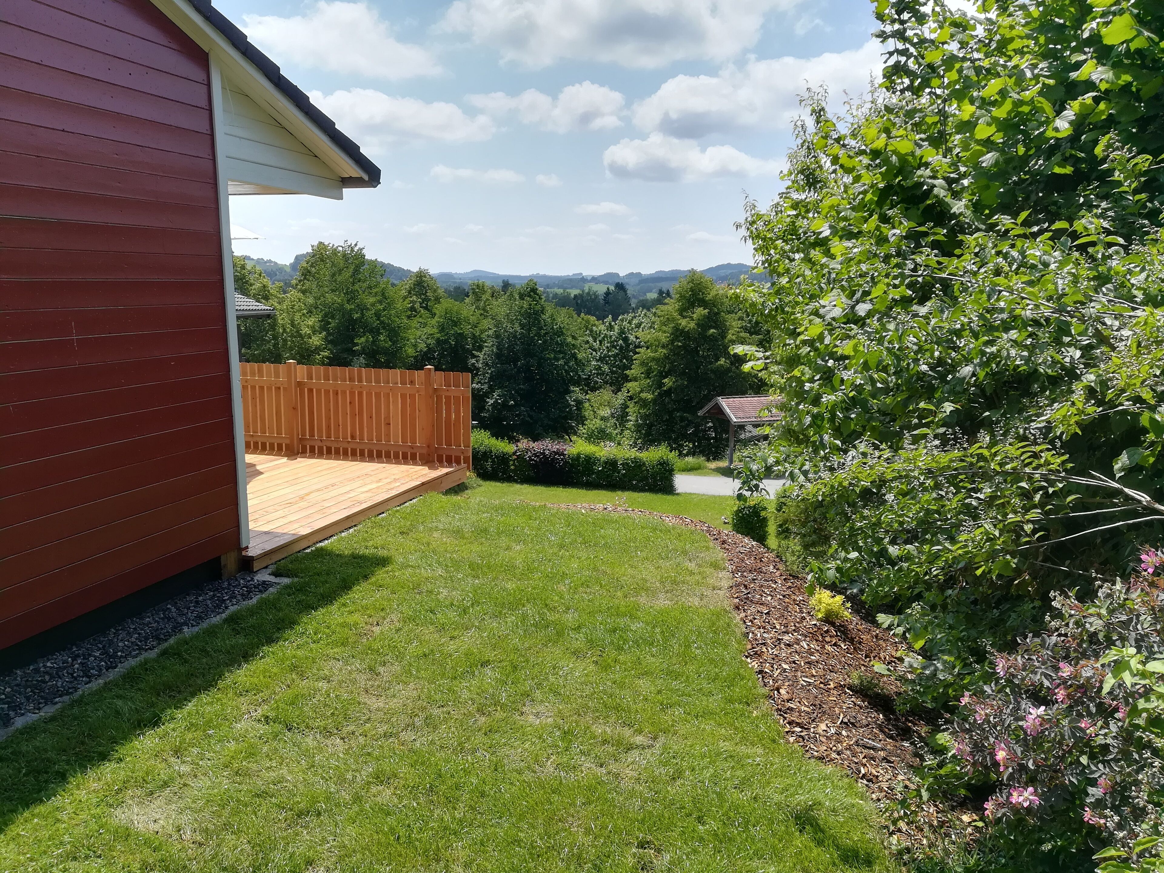 A backyard with a wooden deck, a grassy lawn, and a garden area with shrubs and flowers.