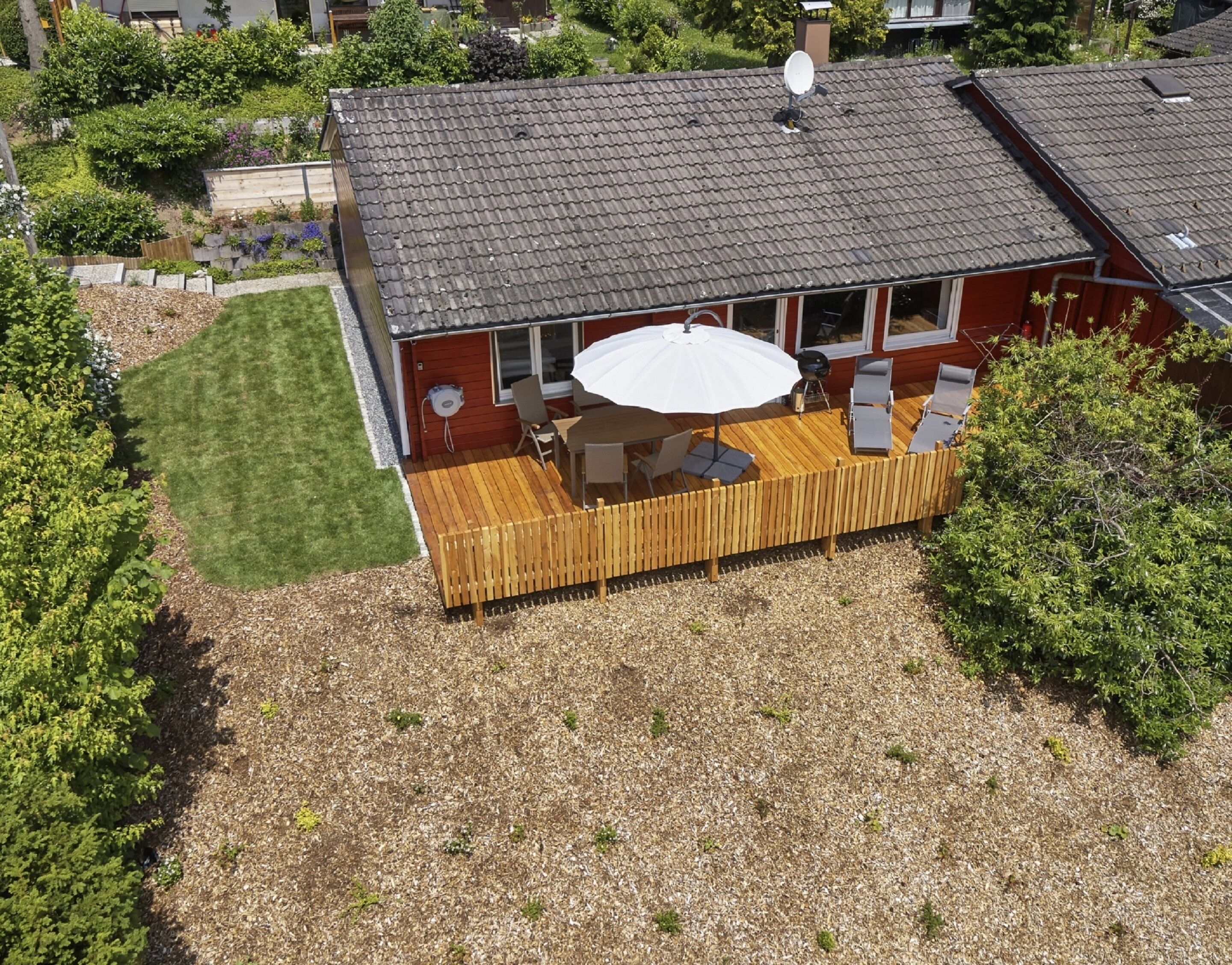 Une terrasse aménagée avec une table et des chaises, entourée d’une clôture en bois et d’une pelouse verdoyante.