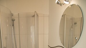 A bathroom with a glass-enclosed shower, a sink, and a mirror. - Pension Jederzeit (Wallersdorf)