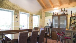 A dining area with wooden furniture, a bar area with bottles, and large windows. - Pension Jederzeit (Wallersdorf)