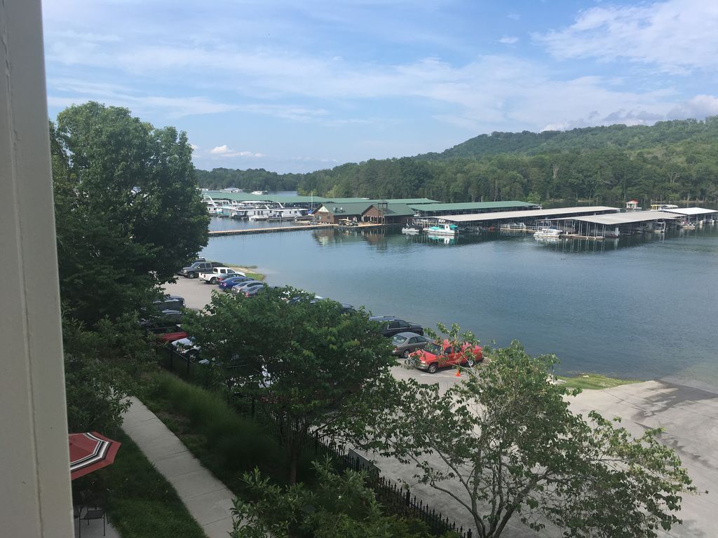 A marina with boats docked, a parking area with cars, and a building with a green roof.