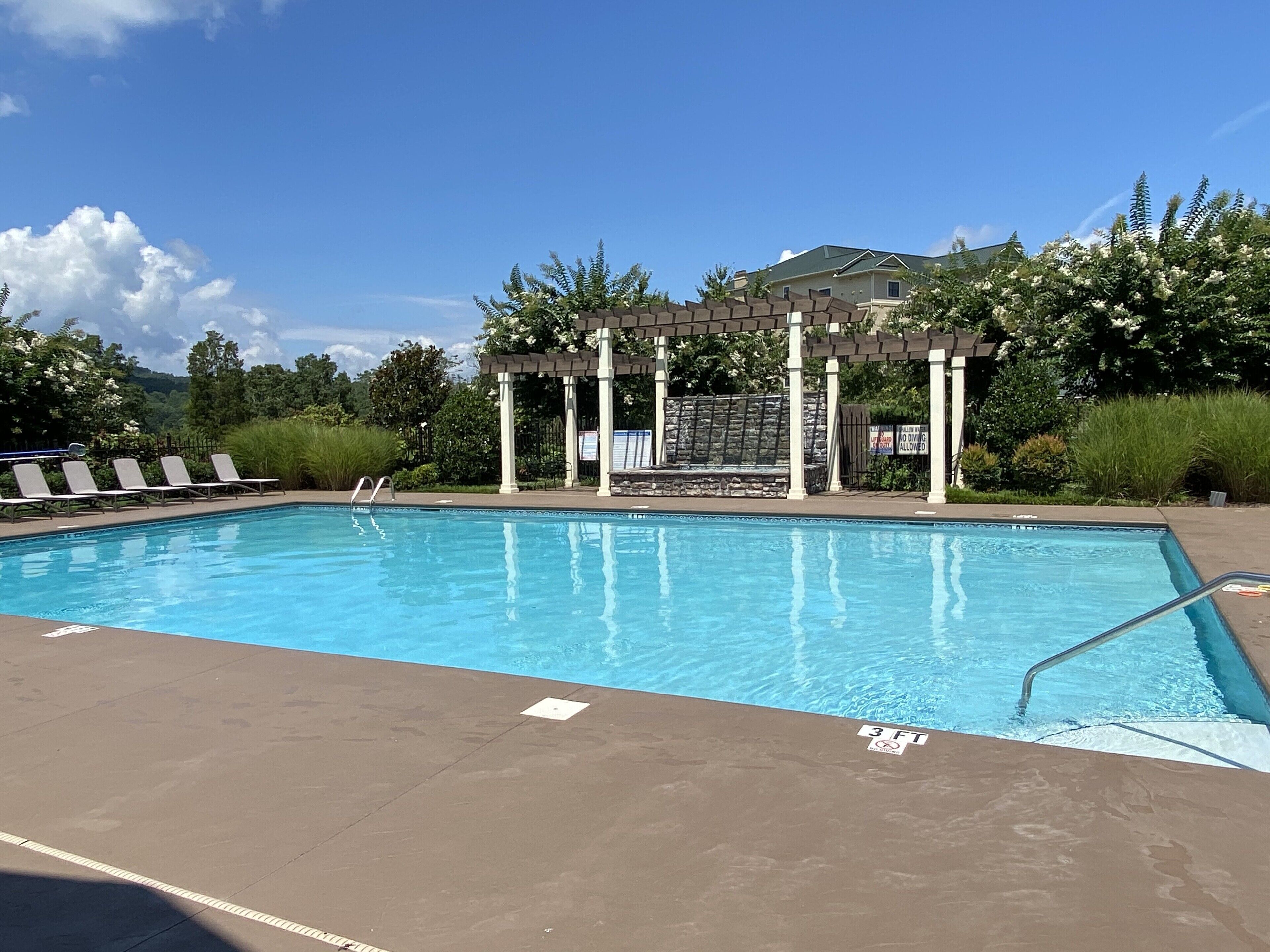A swimming pool with a pergola, lounge chairs, and a lifeguard sign.