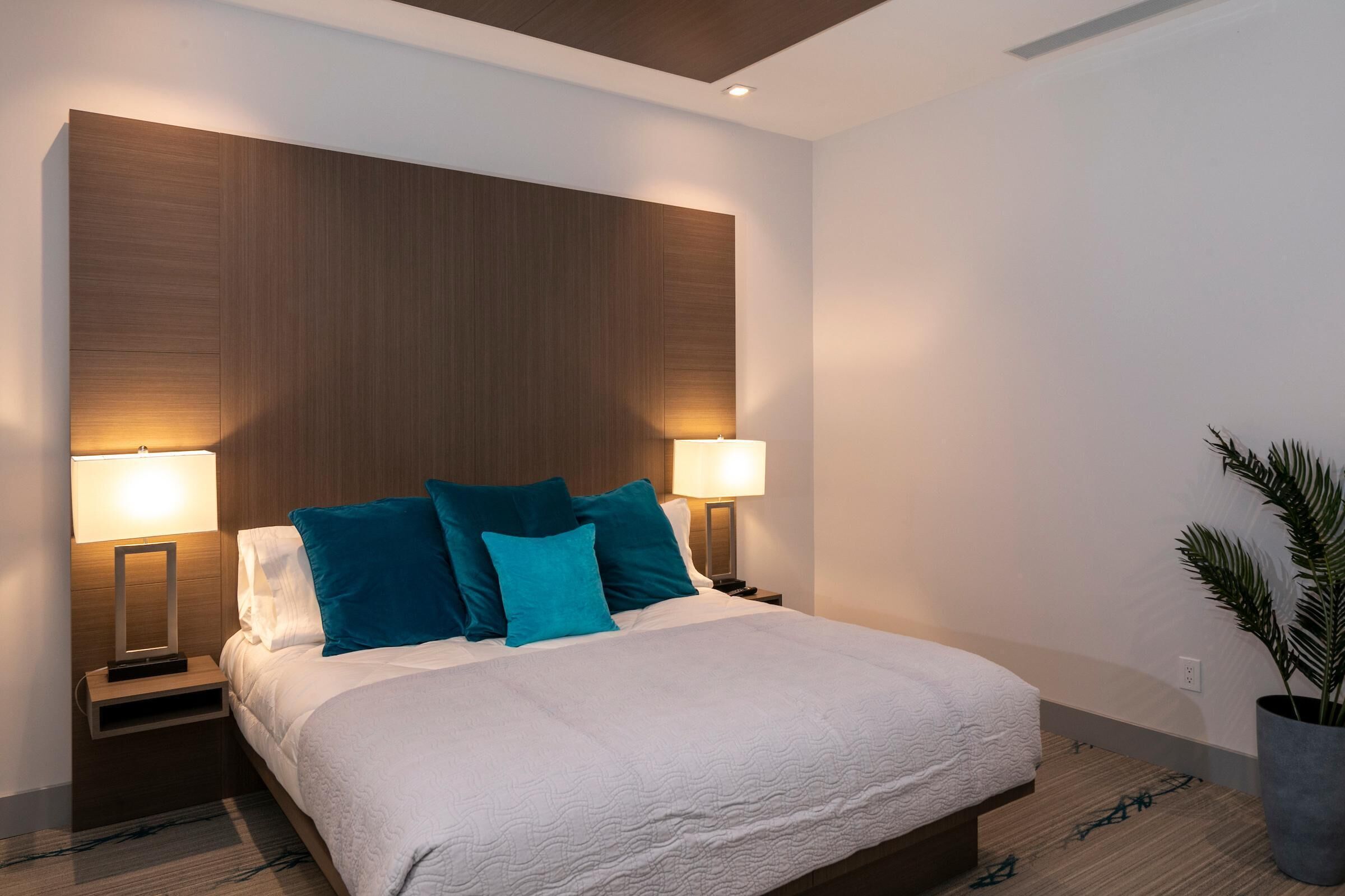 Ein modernes Hotelzimmer mit einem großen Bett, zwei Nachttischen und einem Beistelltisch mit einer Lampe.