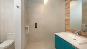 A modern bathroom with a white toilet, a glass shower enclosure, a white sink with a wooden vanity, and a large mirror. - Suite 11 with Large Bathroom (Cruz Bay)