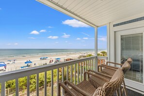 A balcony with wicker furniture overlooking a beach with umbrellas and people. - Direct OCEANFRONT condo, completely renovated, sleeps 7 (Surfside Beach)